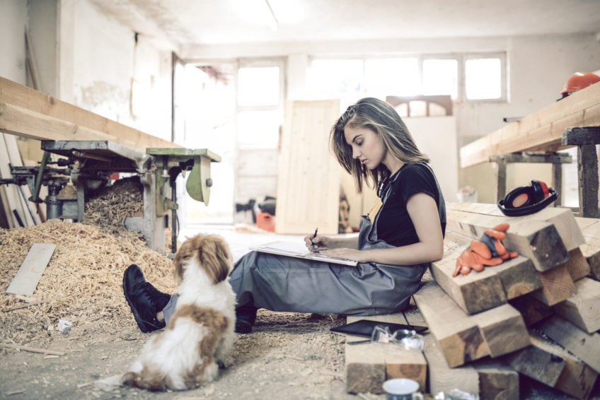 Female Carpenter Designing And Drawing New Project Ideas With Pet Puppy