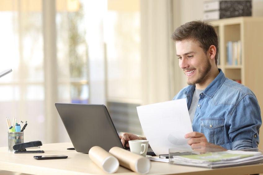 Entrepreneur working with a laptop and holding a document in a little office or home